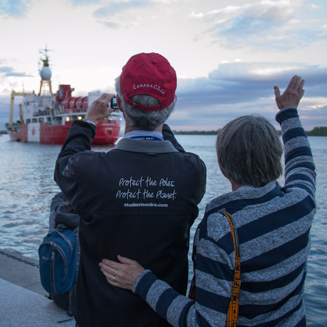 Two people wave farewell to a departing Polar Prince boat from shore at the Canada C3 launch on June 1st in Toronto. Photo credit: Mary Paquet